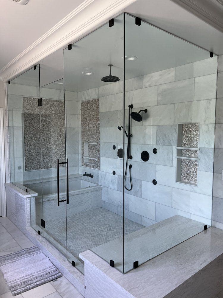Large frameless glass shower enclosure in a marble-tiled bathroom, with a rain showerhead and a built-in soaking tub