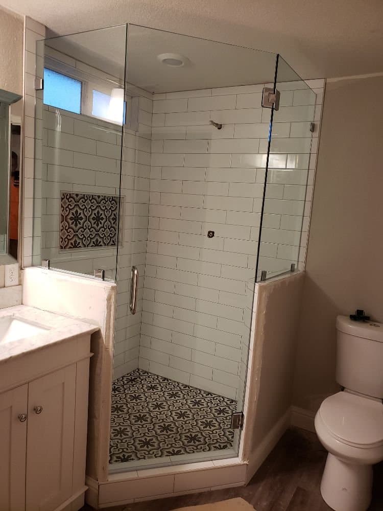 Frameless glass shower enclosure fitted into the corner of a white subway-tiled bathroom with patterned floor tile